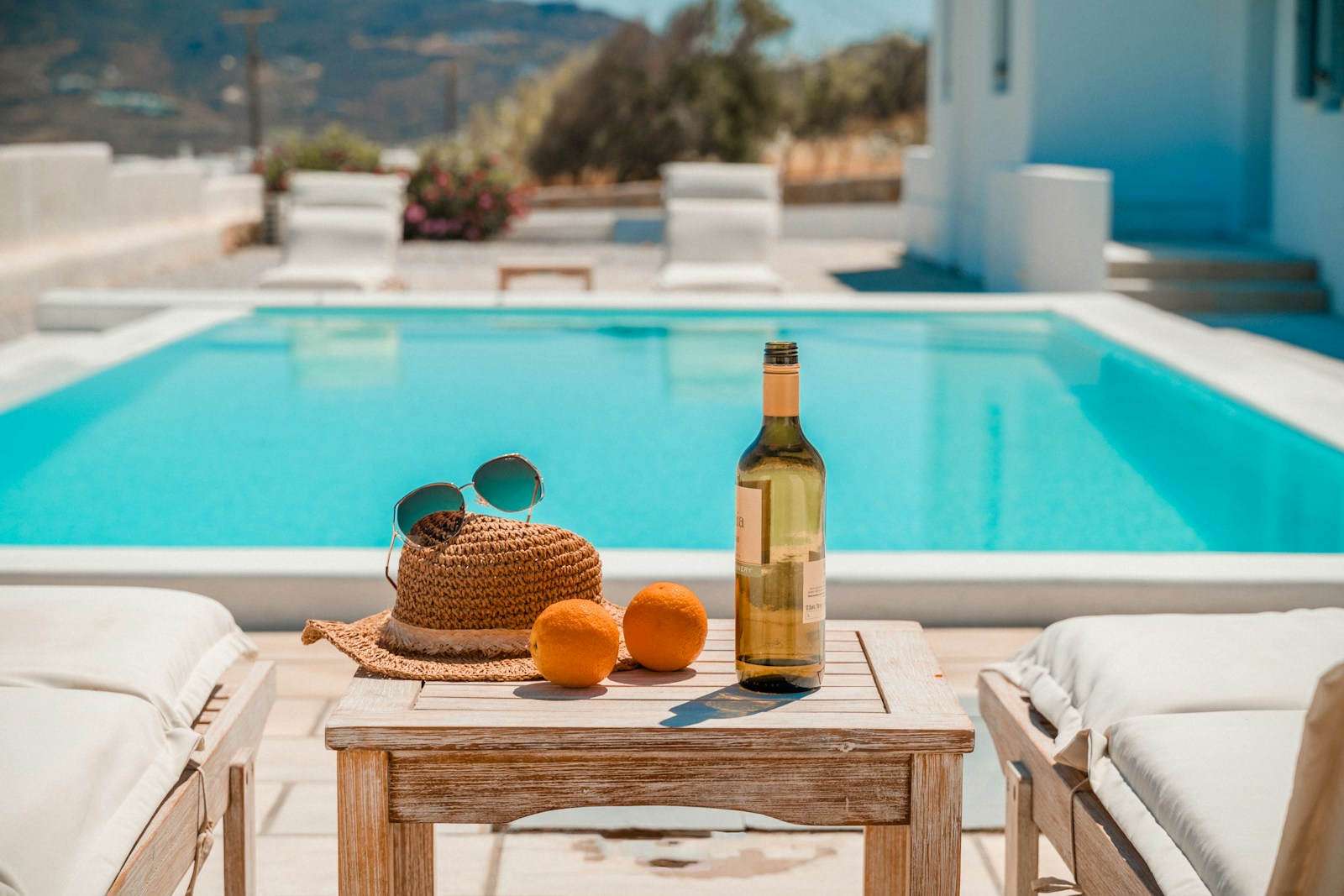 a table with a bottle and a basket of oranges by a pool