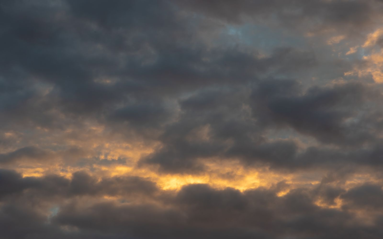 A dramatic cloudy sky with sun peeking through at sunrise, showcasing nature's beauty.