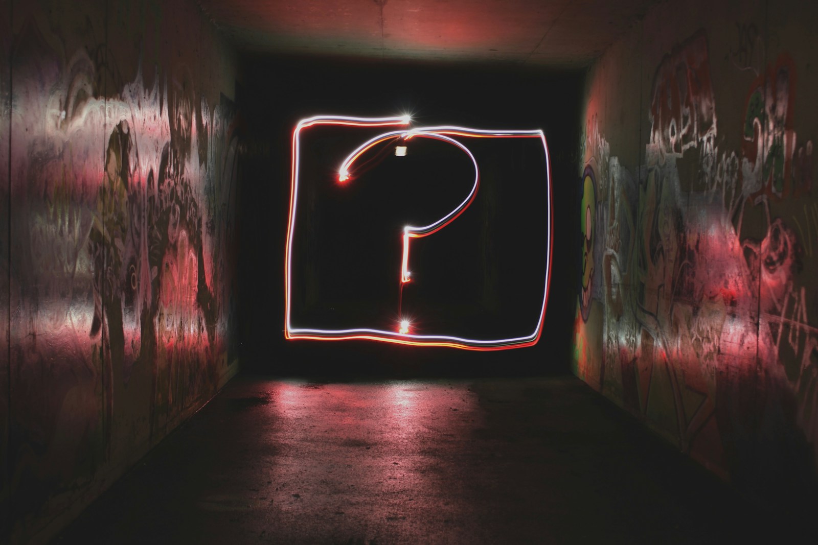 A question mark drawn in light in a dark graffiti covered tunnel