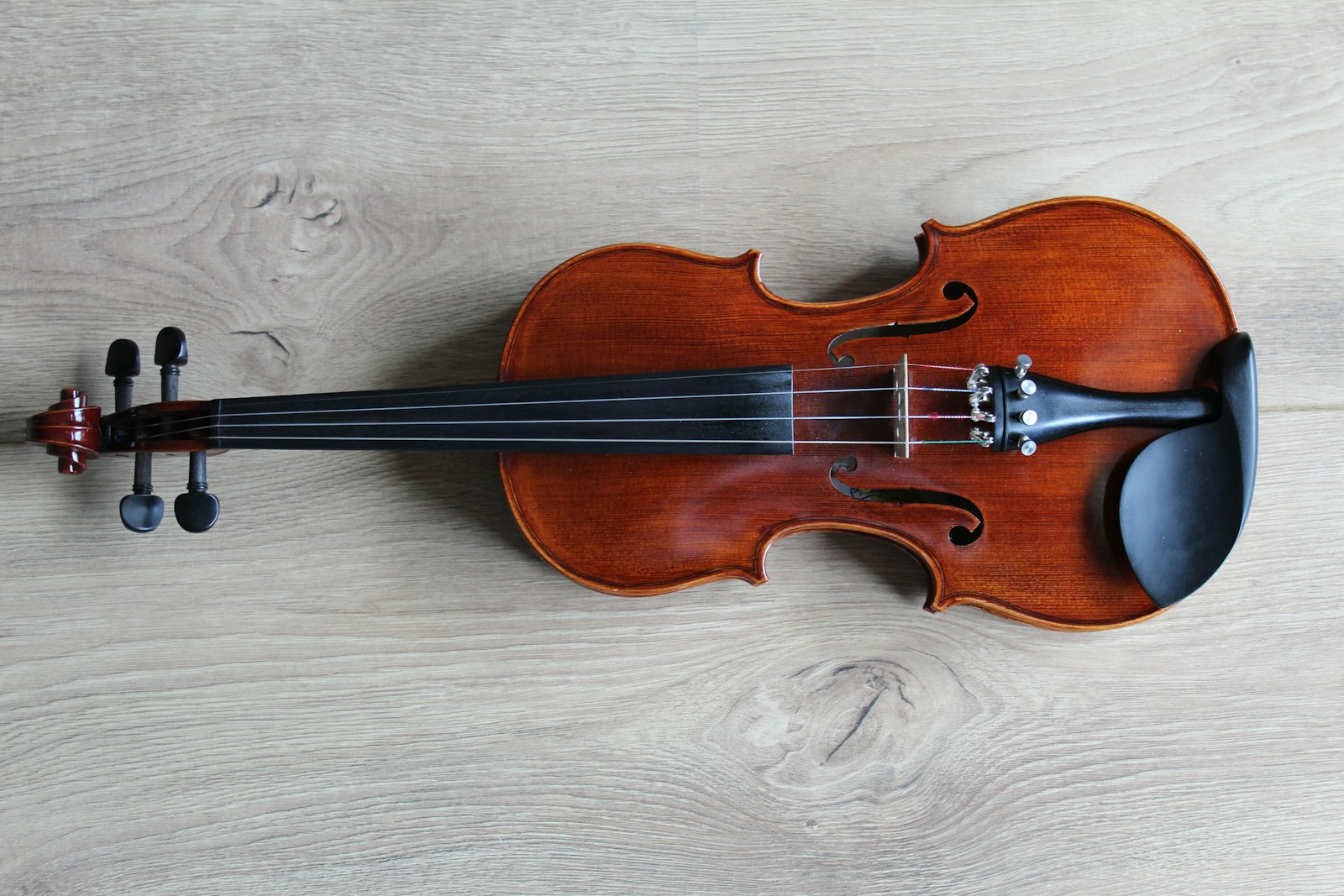 A brown wooden violin with black fittings on a light wood surface