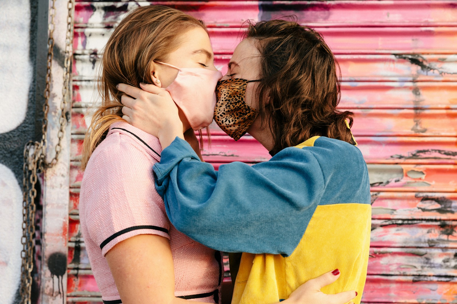 girl in blue and yellow hoodie kissing woman in white shirt